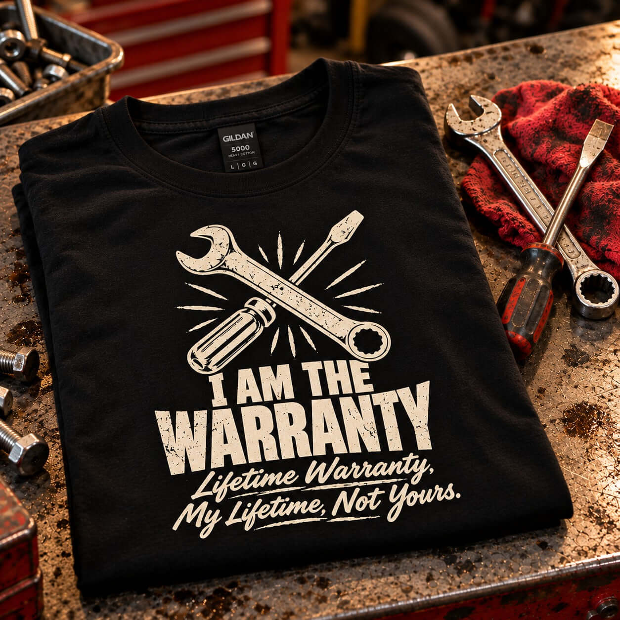 I Am the Warranty T-Shirt - folded black tee on a garage workbench