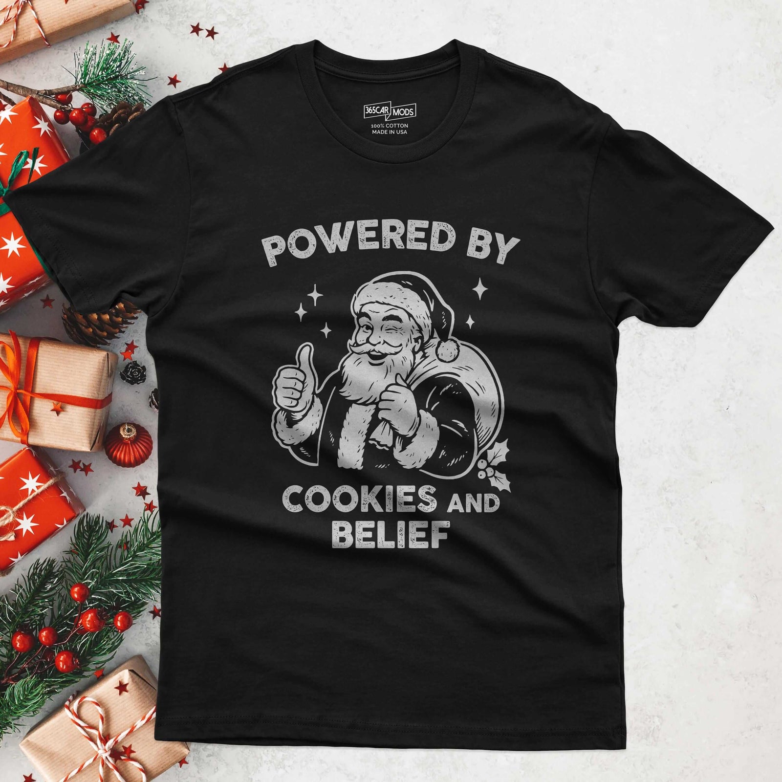 Black t-shirt with a graphic of Santa Claus giving a thumbs up next to a sack of gifts and the text POWERED BY COOKIES AND BELIEF.