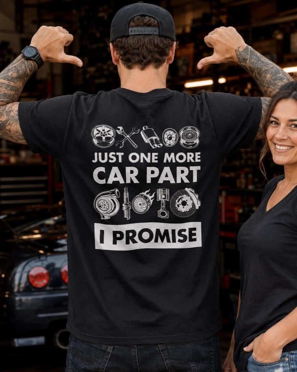 Man pointing to a Just One More Car Part graphic on a black T-shirt outside his home garage.