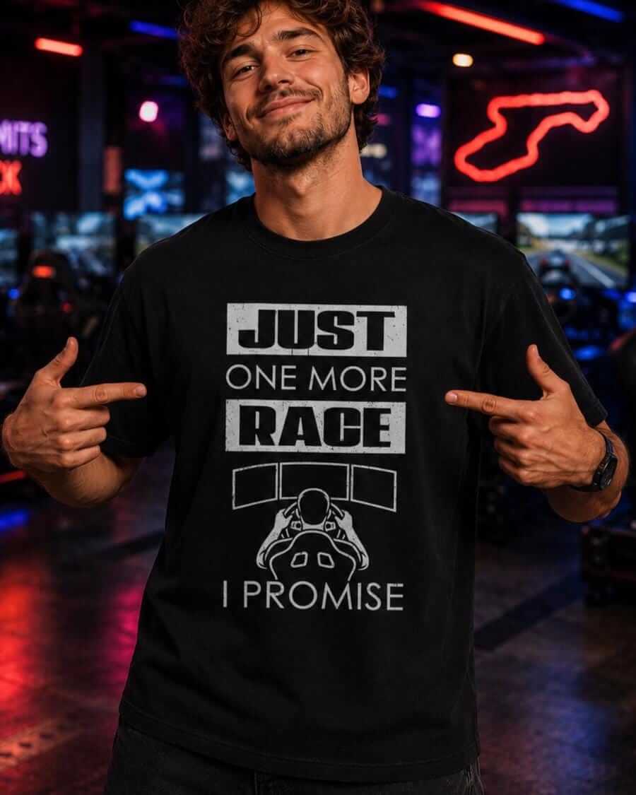Young sim racer wearing a black “Just One More Race, I Promise” T-shirt and pointing to the design inside a neon-lit racing simulator arcade.