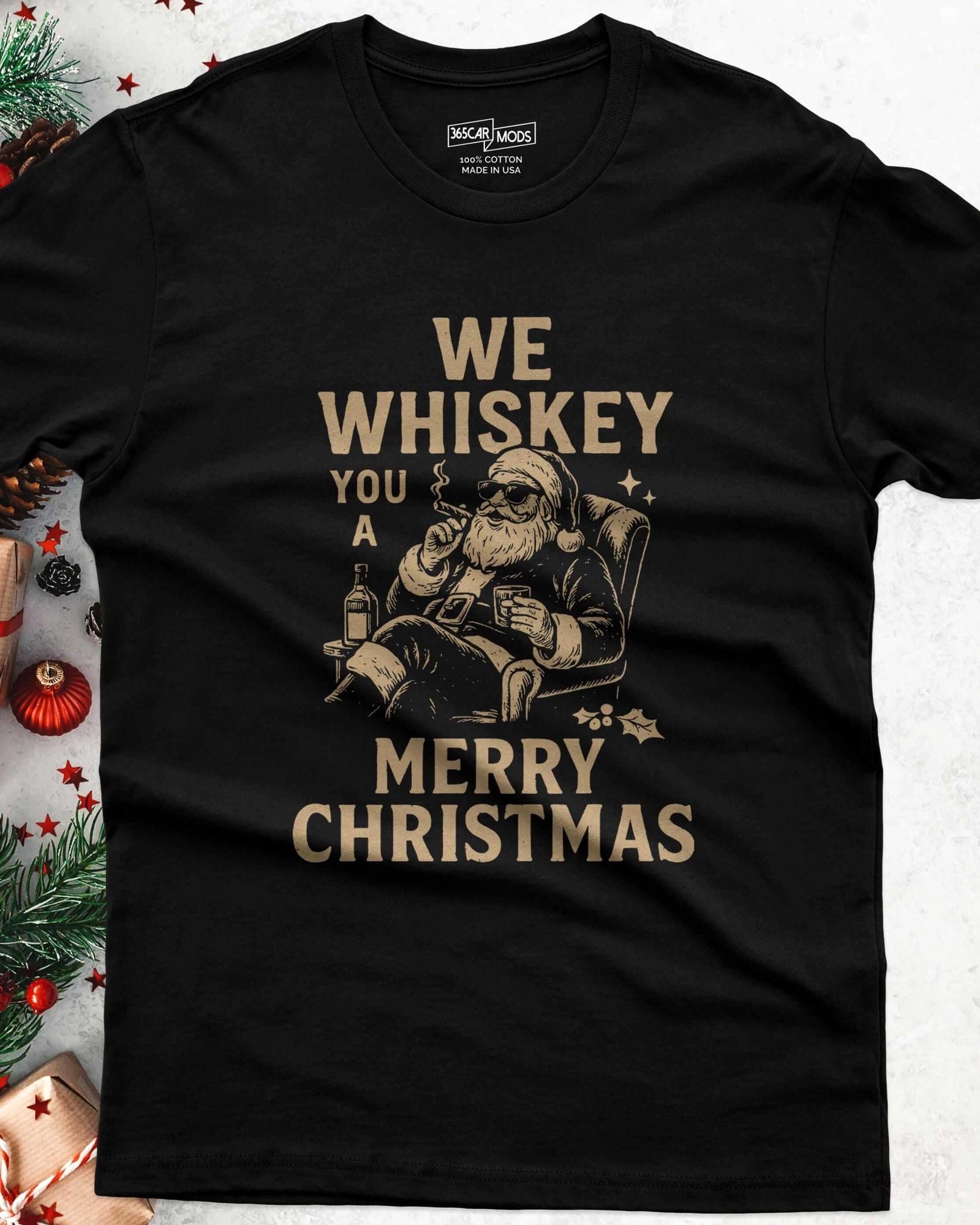 A black short-sleeve t-shirt featuring a graphic of Santa Claus wearing sunglasses, sitting in a chair, holding a glass and a cigar. The text reads: WE WHISKEY YOU A MERRY CHRISTMAS.