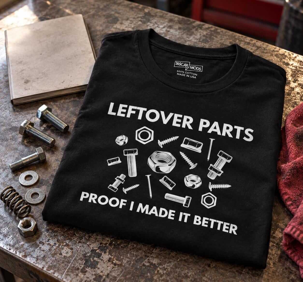 Folded black Leftover Parts shirt on a workbench next to a pile of extra bolts, washers and a spring