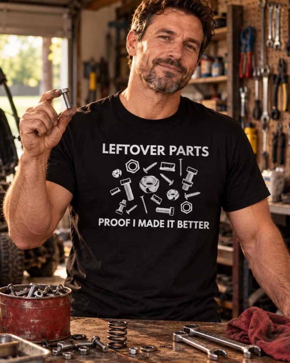 Man at a garage workbench holding up a leftover bolt, wearing a black Leftover Parts Proof I Made It Better shirt