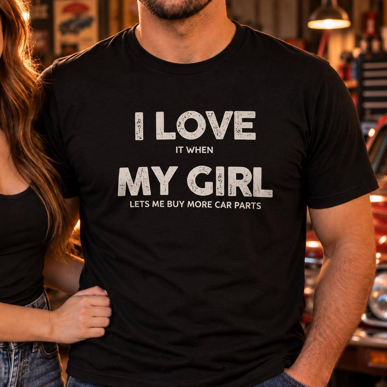 Close-up of a man in a black I Love My Girl car parts shirt with his girlfriend's arm around his waist