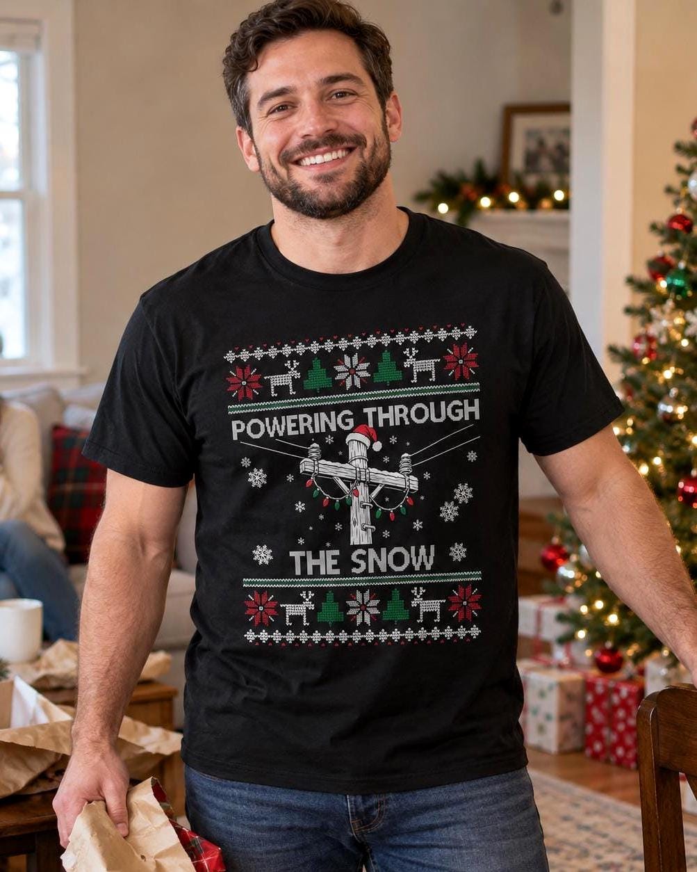 Powering Through the Snow Lineman Christmas T-Shirt - lineman wearing the black tee by a Christmas tree
