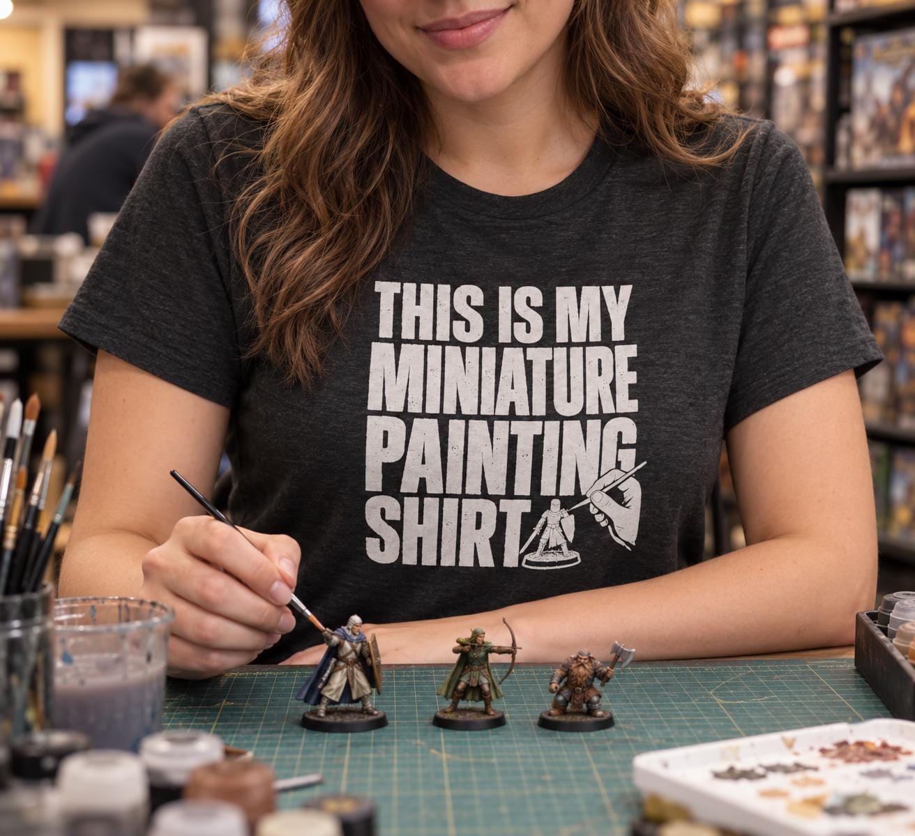 This Is My Miniature Painting Shirt - woman in the dark heather t-shirt painting miniatures at a game store table