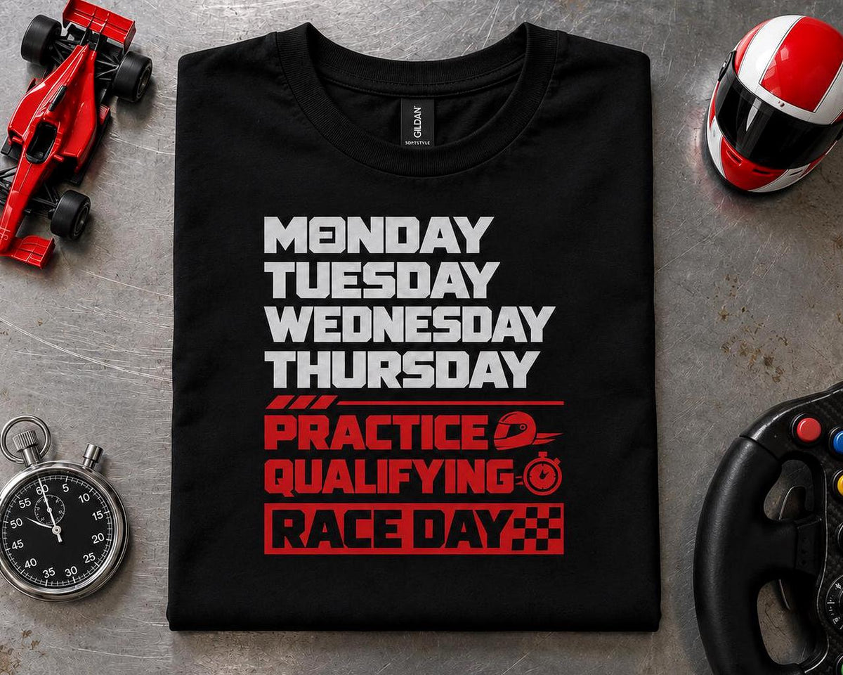 Race Weekend T-Shirt - black t-shirt folded on a garage floor next to a toy race car, a helmet, a stopwatch and a steering wheel