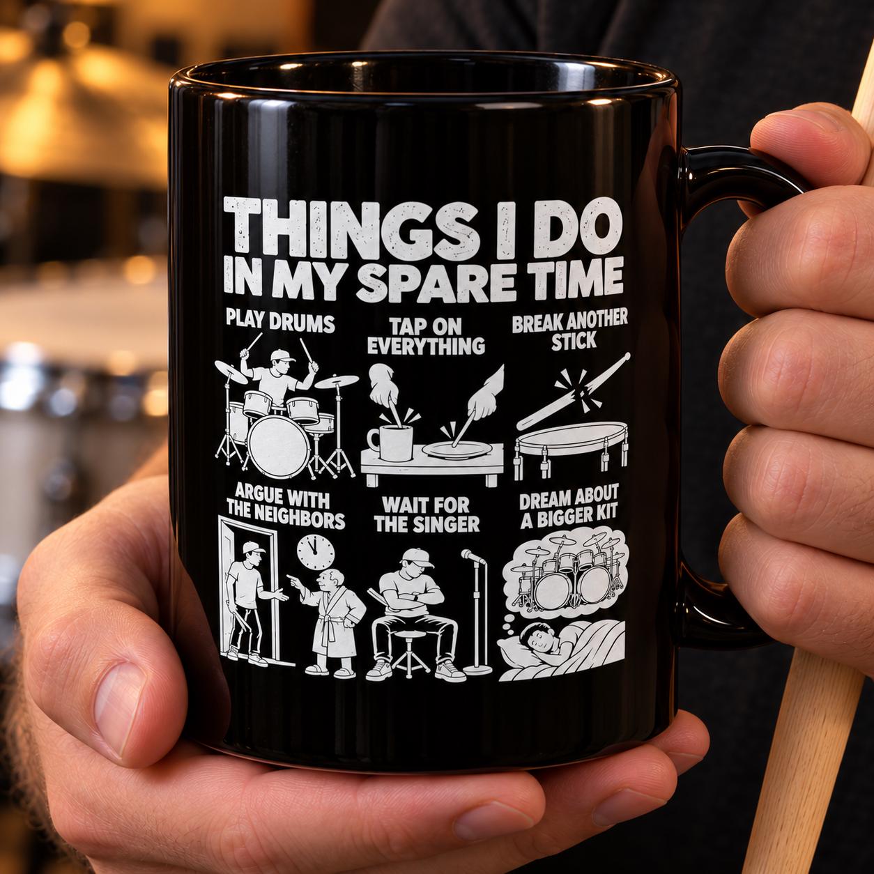 Hand holding the black Things I Do In My Spare Time drummer mug with a drumstick in a rehearsal room
