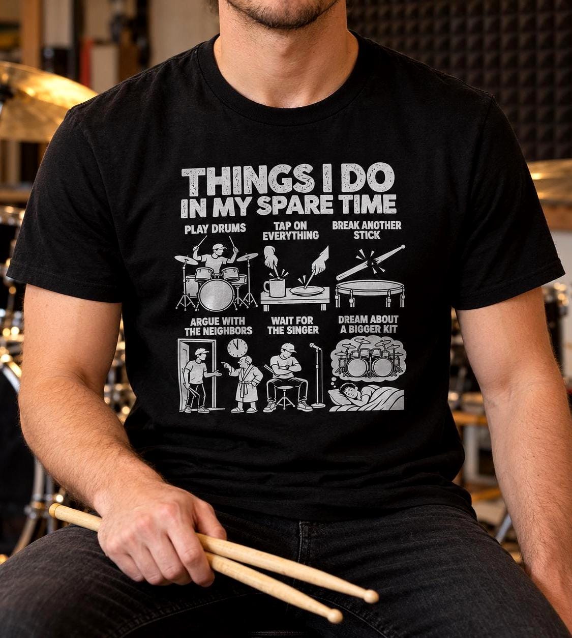 Drummer in the black spare time t-shirt holding drumsticks in a rehearsal room