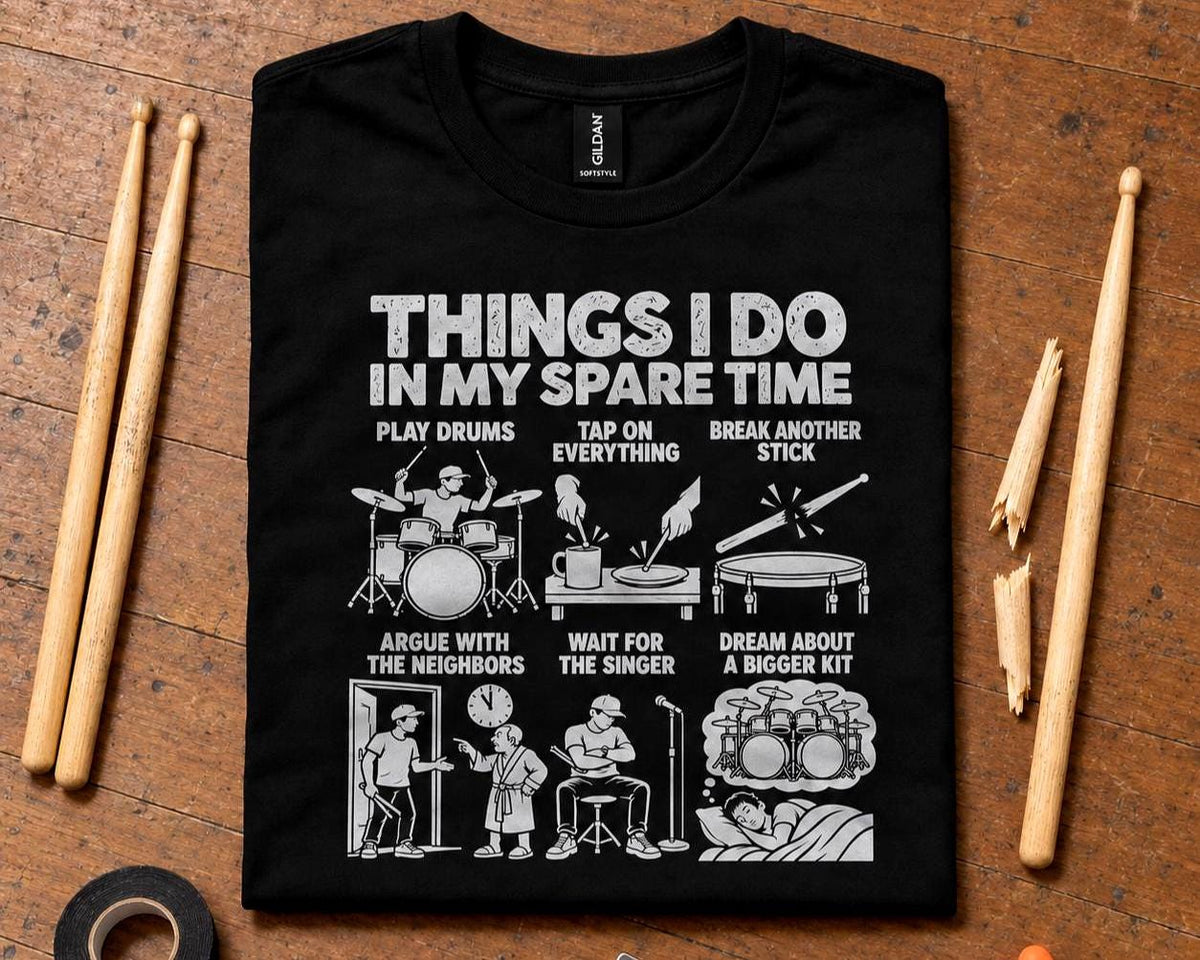 Black drummer spare time t-shirt laid flat on a wooden floor with drumsticks and a broken stick