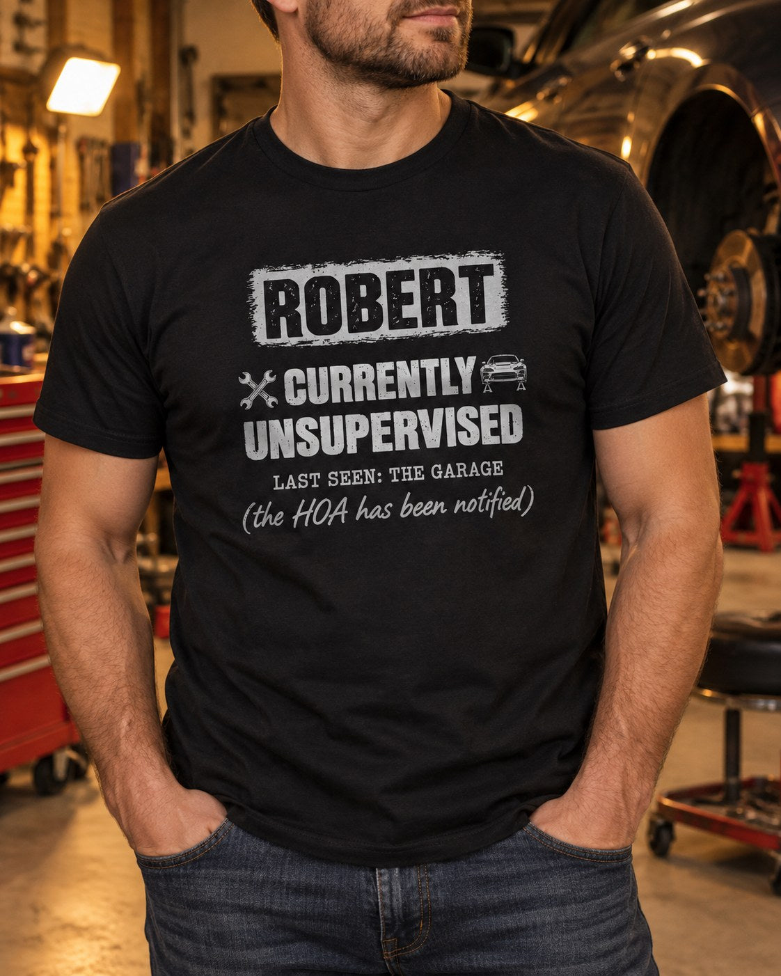 Man wearing the black personalized Currently Unsupervised car guy t-shirt in a garage