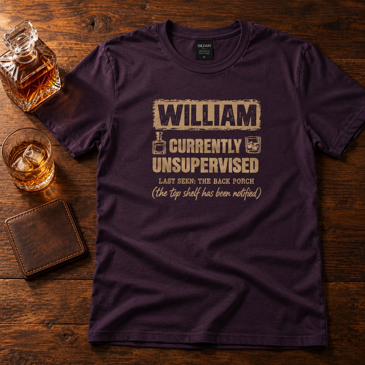 Blackberry personalized Currently Unsupervised whiskey t-shirt on a wooden table with whiskey and a leather wallet