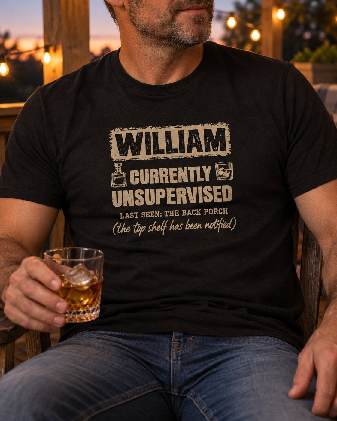 Man in the black personalized Currently Unsupervised whiskey t-shirt holding a glass of whiskey on the back porch