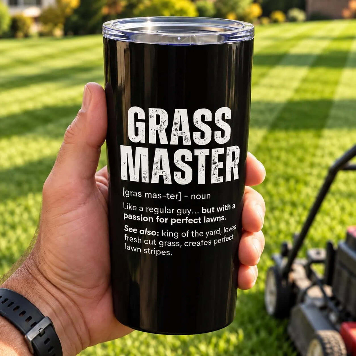 Hand holding the black Grass Master Definition 20oz tumbler over a freshly striped lawn, lawn mower in the background