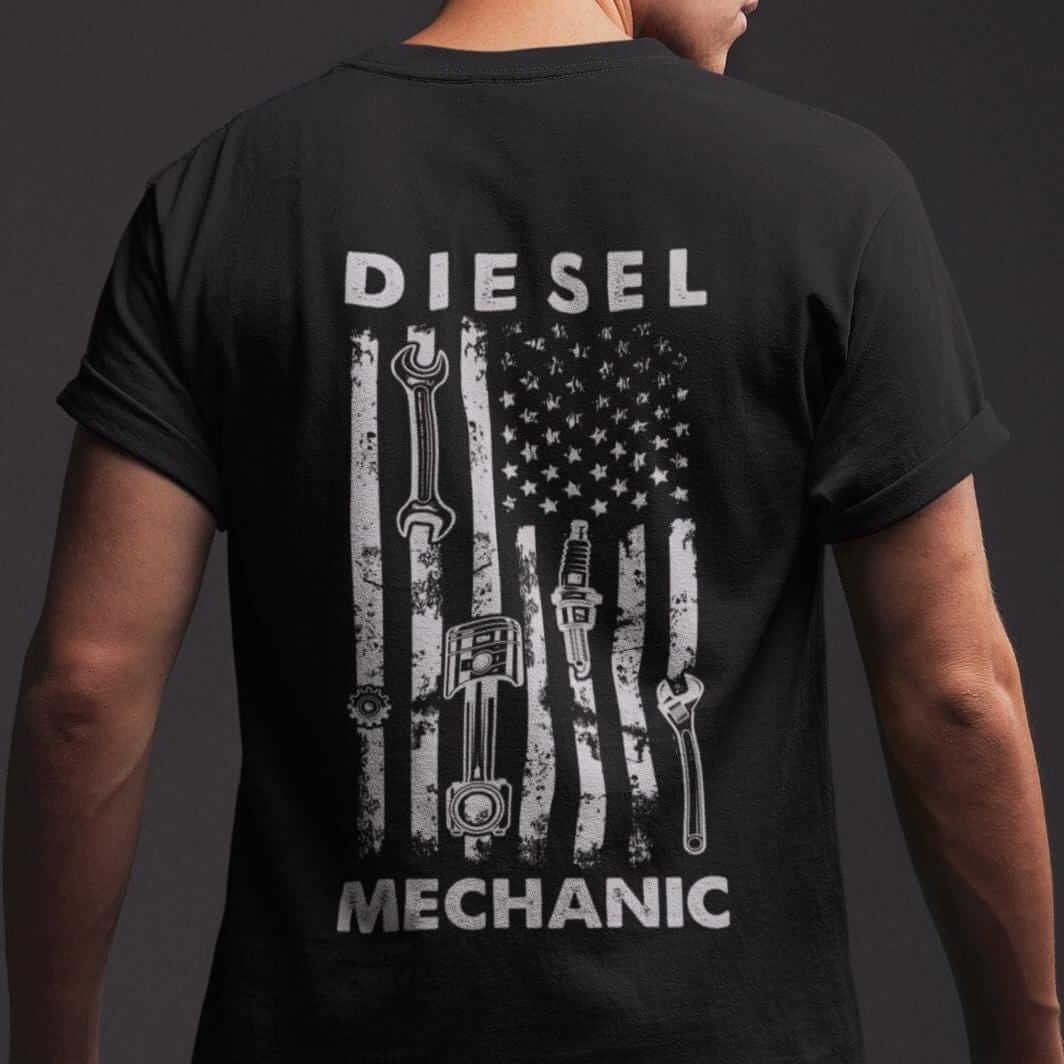 Black t-shirt with a white distressed American flag design. The flag has various tools printed on it, including wrenches, spark plugs, and a piston. The text "DIESEL MECHANIC" is printed above and below the flag.