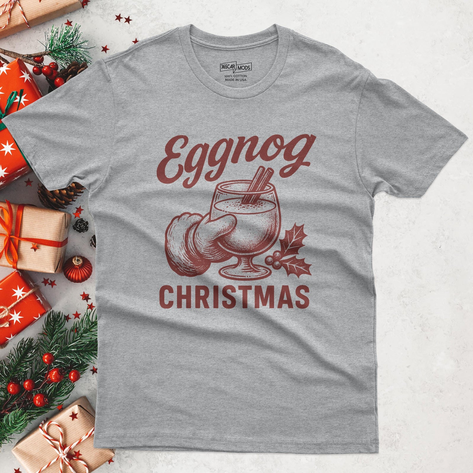 A heather gray t-shirt with a festive design. The graphic features the word "Eggnog" in a stylized font, along with an illustration of an eggnog drink in a glass, a nutmeg, and the word "Christmas".