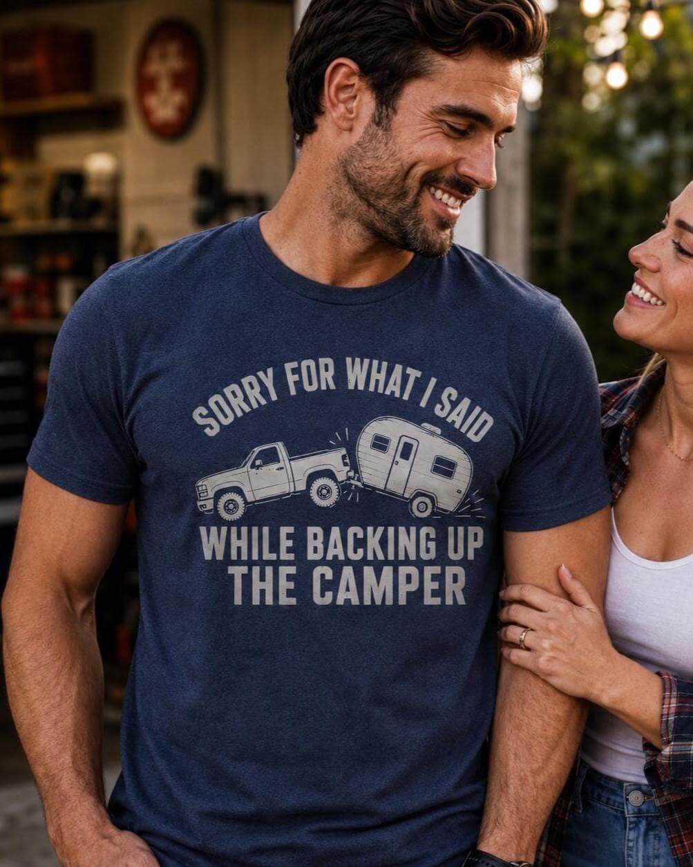 A heathered navy blue short-sleeve t-shirt featuring a graphic of a pickup truck towing a camper trailer. The text printed in light gray reads: SORRY FOR WHAT I SAID WHILE BACKING UP THE CAMPER.