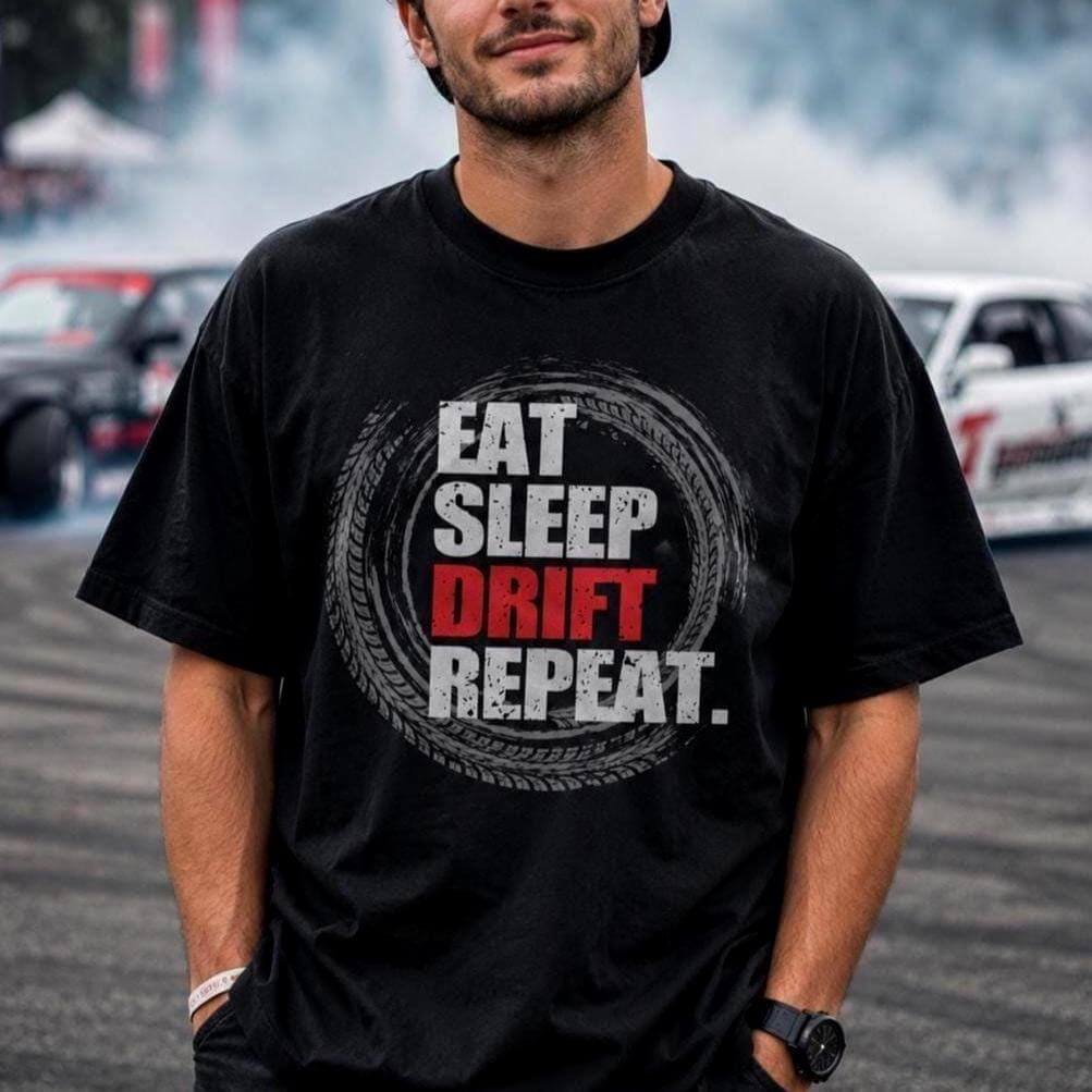 Black oversized drift-themed T-shirt worn by a smiling young man in a backward cap, with drifting JDM cars and smoke blurred in the background.