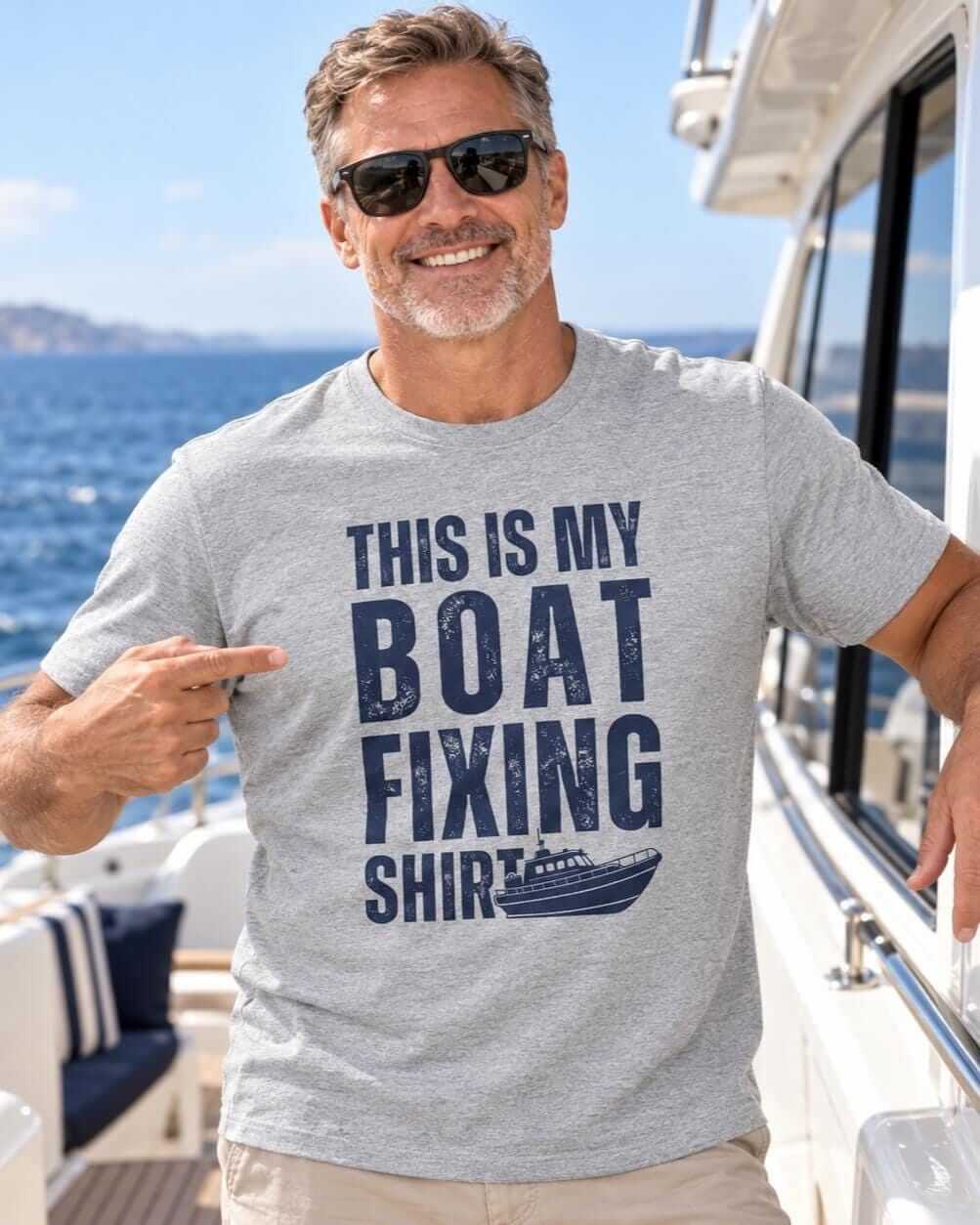 Smiling mature man in sunglasses wearing a sports grey “This Is My Boat Fixing Shirt” T-shirt aboard a yacht with the blue sea behind him.
