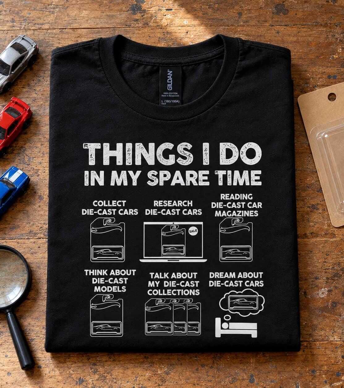 Folded black die cast car collector t-shirt on a table next to loose die cast cars and a magnifying glass