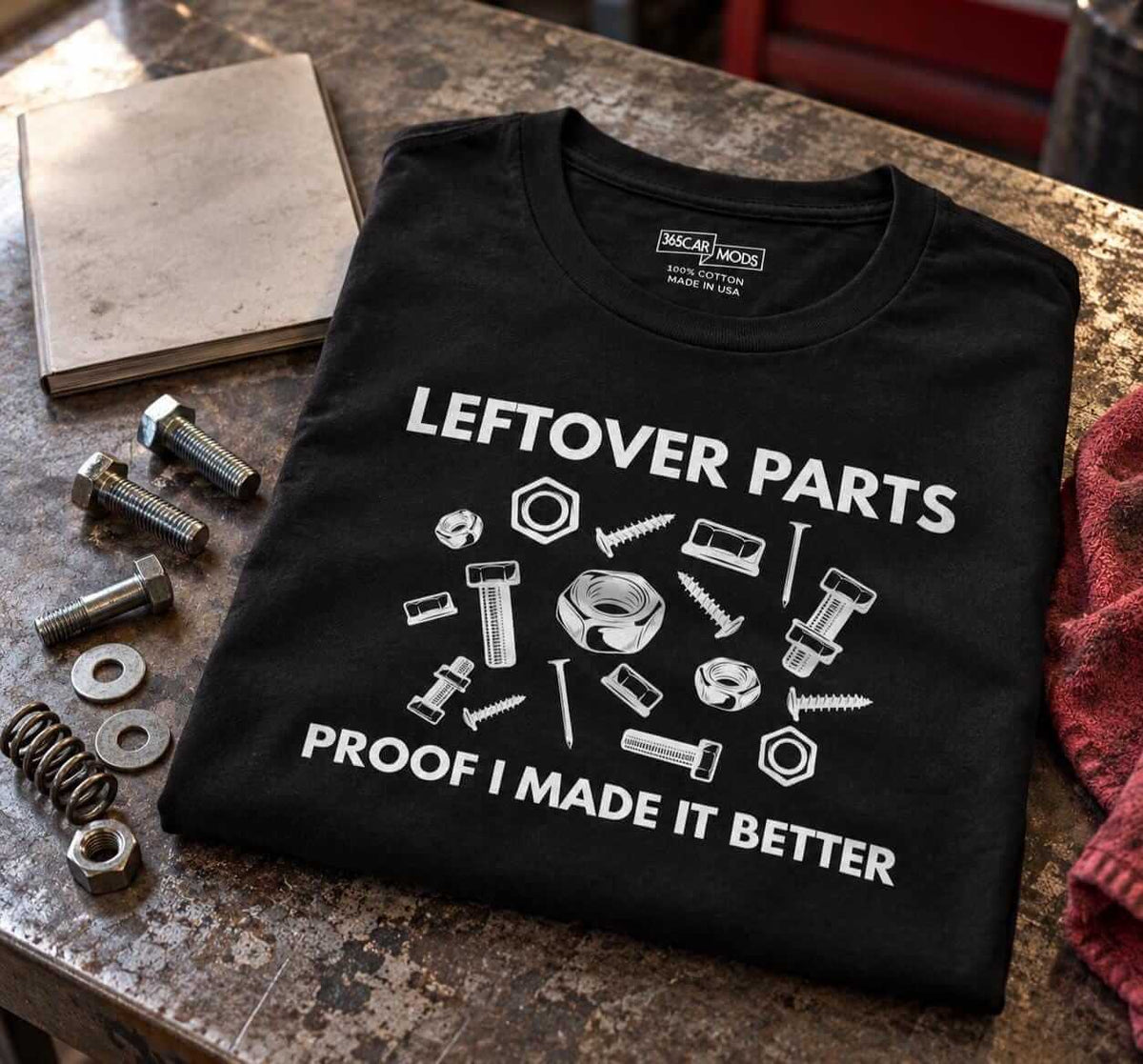 Folded black Leftover Parts shirt on a workbench next to a pile of extra bolts, washers and a spring