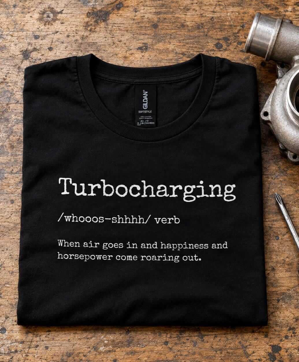 Folded black turbocharging definition t-shirt on a workbench next to a turbocharger and a boost gauge