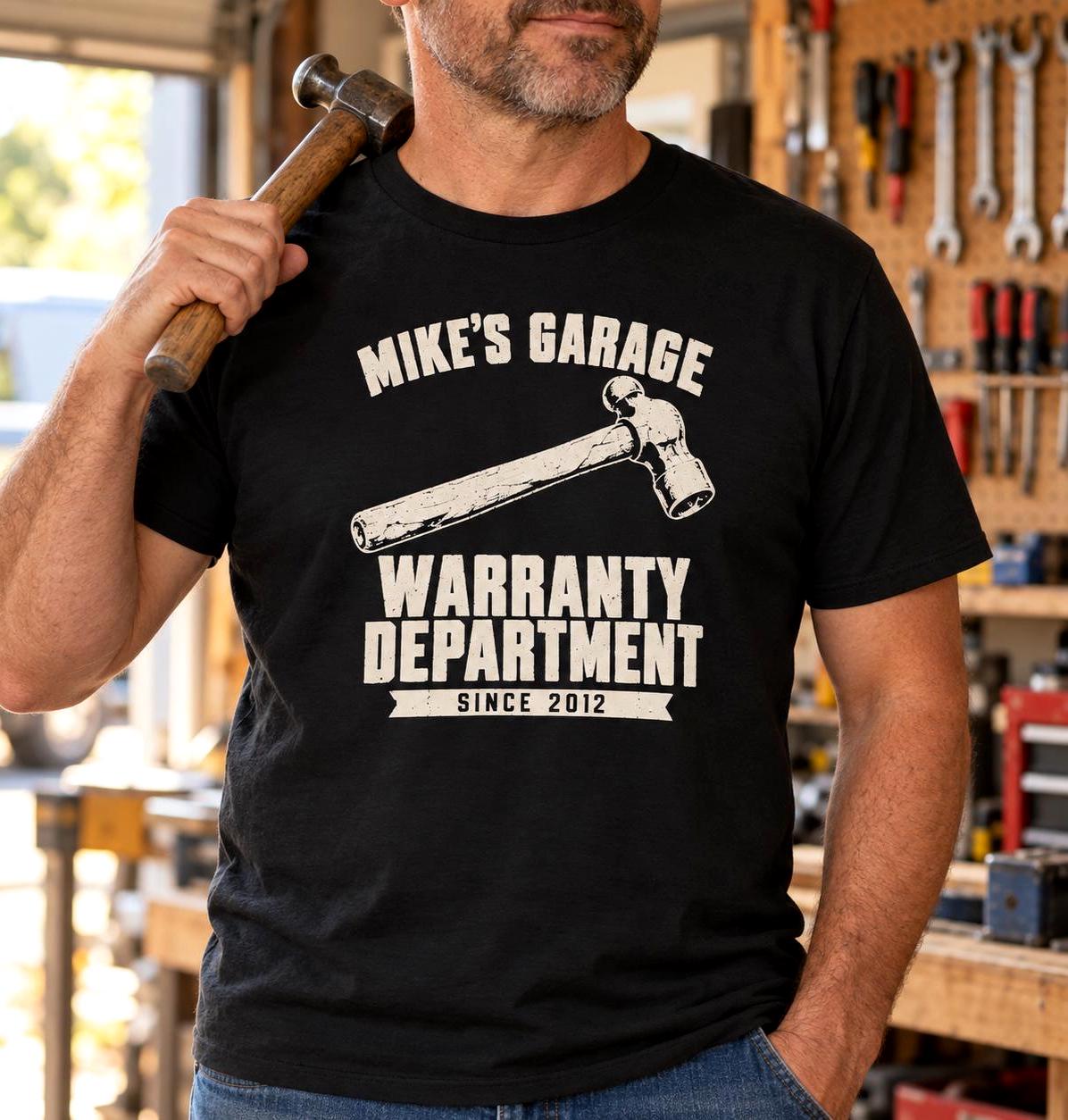 Man in a home garage wearing the black personalized Warranty Department t-shirt with a hammer on his shoulder