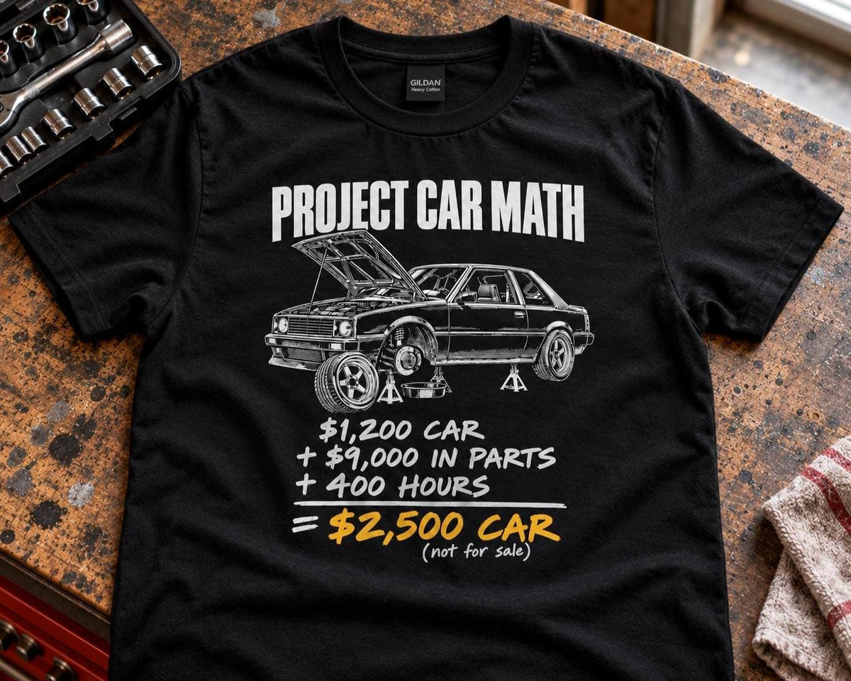 Black Project Car Math t-shirt laid out on a garage workbench next to a brake rotor