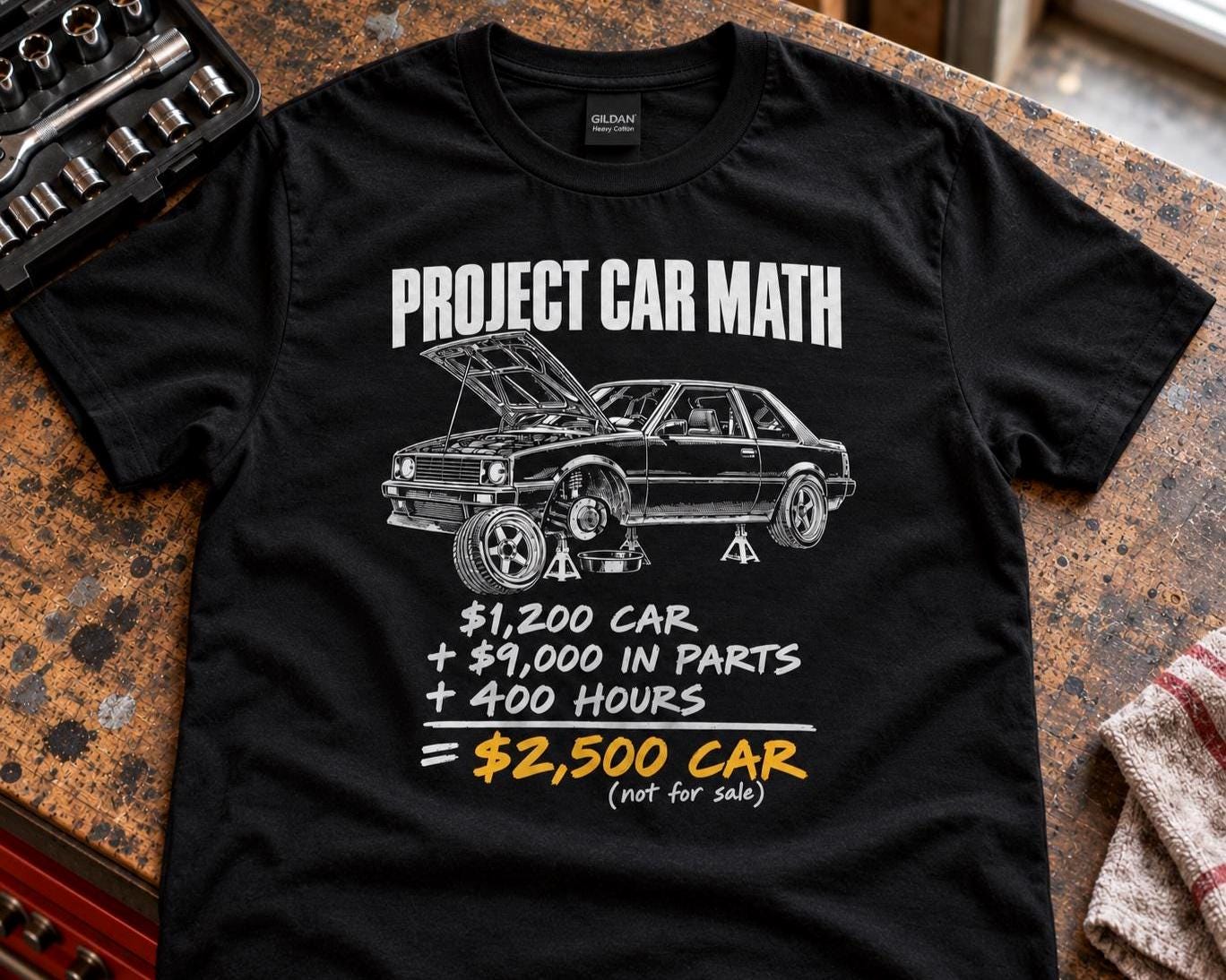 Black Project Car Math t-shirt laid out on a garage workbench next to a brake rotor