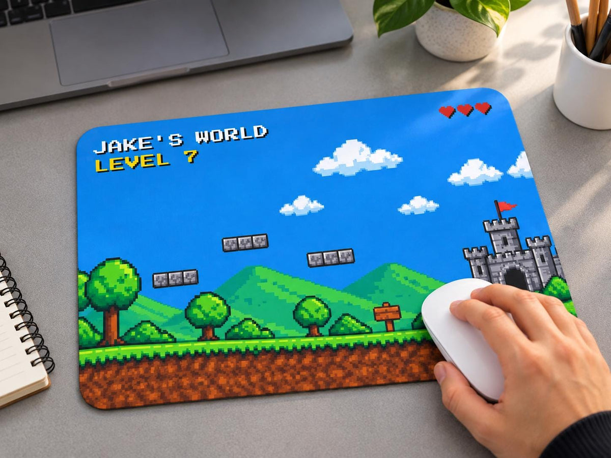 Personalized pixel art mouse pad with JAKE'S WORLD and LEVEL 7, a hand on a white mouse next to a laptop
