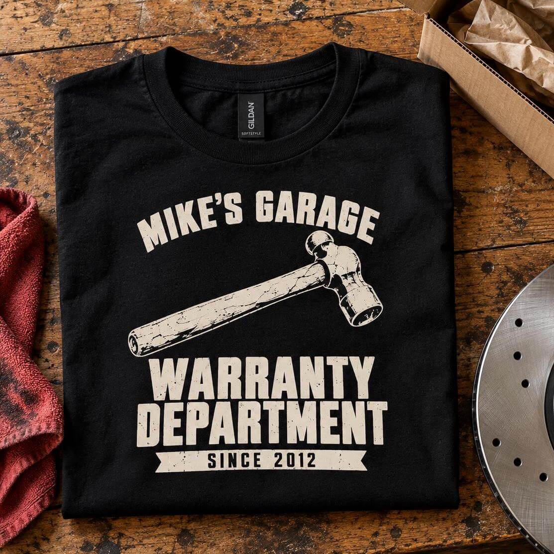 Black Warranty Department personalized garage t-shirt folded on a workbench in a home garage