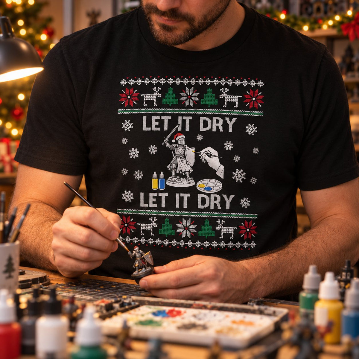 Miniature painter in the black Let It Dry Christmas t-shirt painting a knight at a hobby desk full of paints