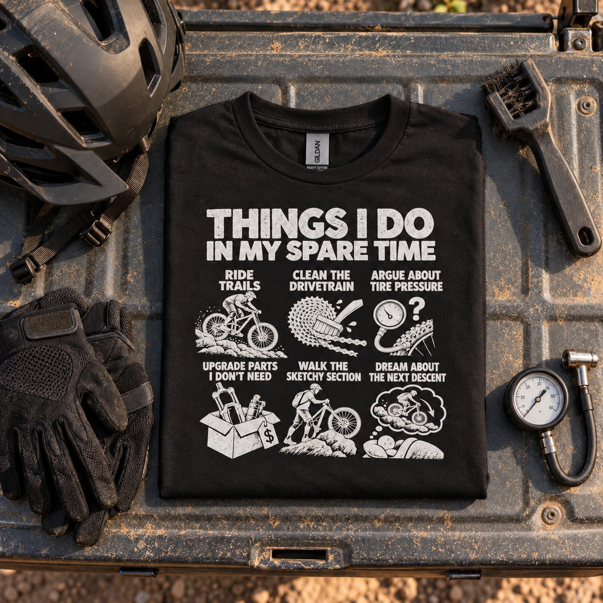 Black mountain bike spare time t-shirt folded on a truck tailgate next to a helmet, riding gloves and a tire pressure gauge